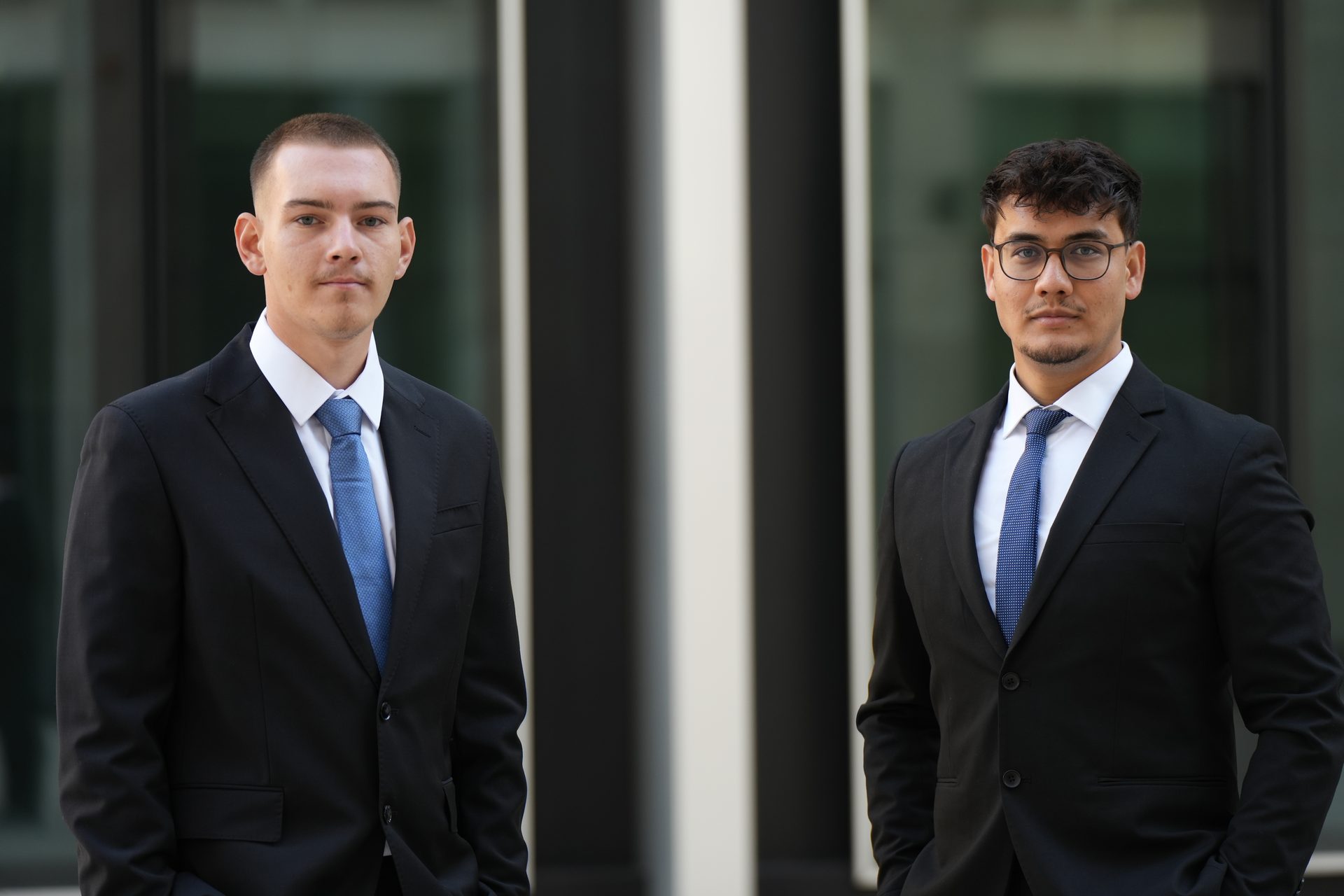 Die Gründer von AHMADI & GEBERT im Anzug vor einer Glasfassade